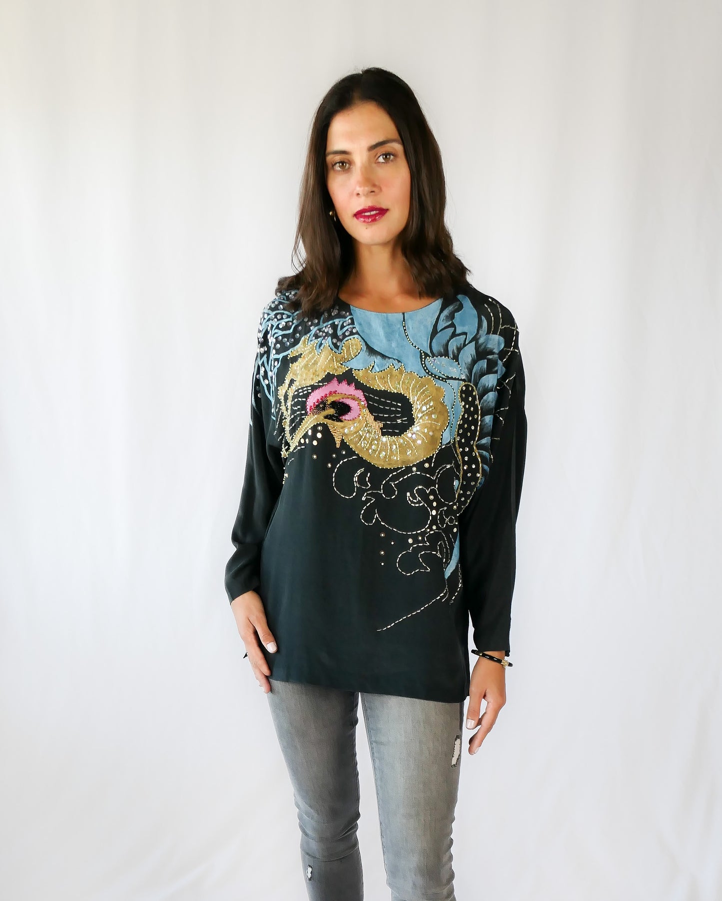 Make a bold party statement in this black silk pullover top with a hand-painted gold and turquoise phoenix, embellished with iridescent, pink, black, and clear colored sequins. In Chinese culture, the phoenix is a symbol of virtue, harmony, balance and peace. This beautifully made top is sure to bring harmony to your wardrobe as well!