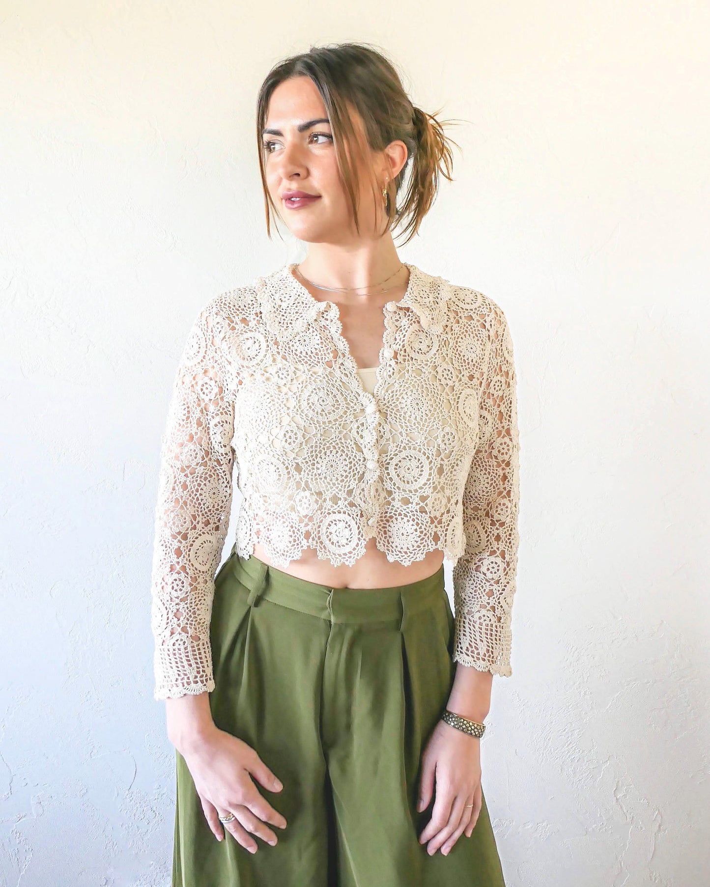 A versatile and boho chic hand crocheted cropped cardigan sweater with a unique, repeating kaleidoscope-like floral pattern throughout. Dress it down with a pair of jeans and sandals, or dress it up with neutral colored wide leg pants, heels, and a pair of vintage dangly earrings.